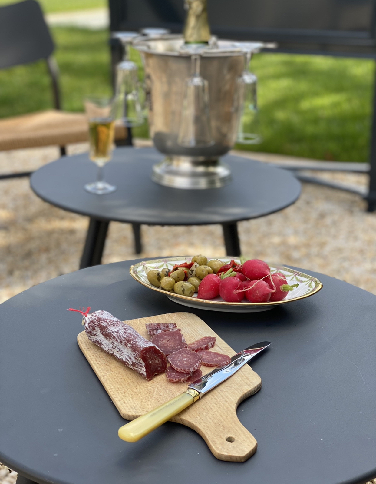 deux tables avec seau à glace et bouteille de champagne avec des planches à découper avec des tranches de saucisson sec et des radis et des olives